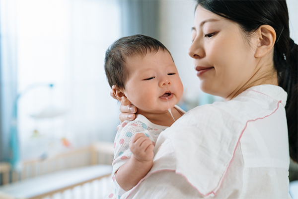 Asian baby spits up milk after mom burps her
