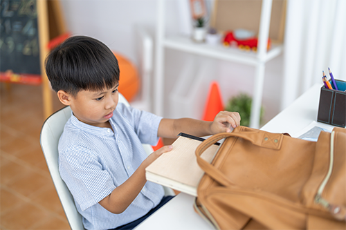 Asian boy looking at textbook in his schoolbag