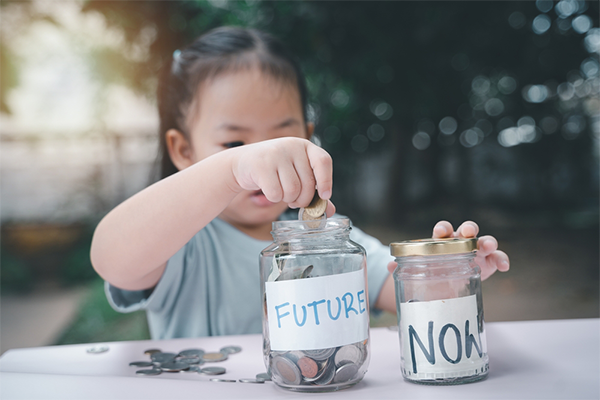 Asian child learns how to save money by dropping her extra coins in jars