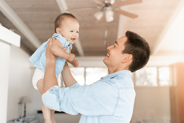 Asian dad lifts his baby daughter while standing in living room