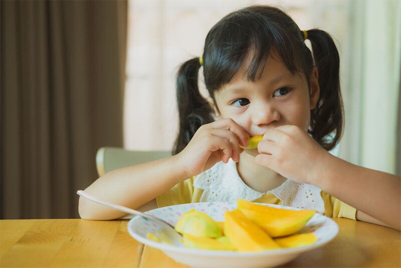 Asian girl of preschool age eats only slices of mangoes for her meal
