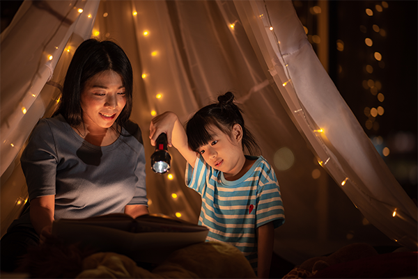 Asian girl playing with a flashlight in an indoor tent and darkened room with her mom