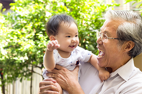 Asian grandfather laughs as his 1-year-old grandson attempts to wave goodbye