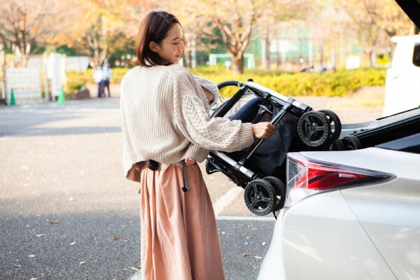 Asian mom carrying her baby takes out a stroller from the trunk of a car