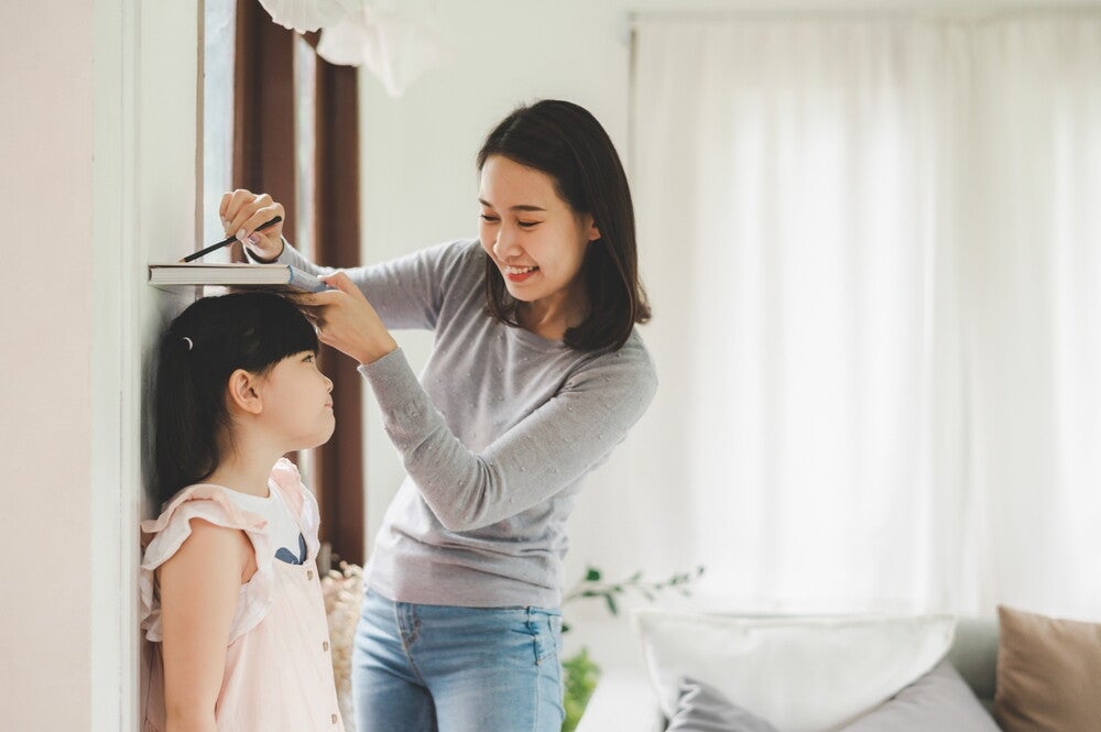 Asian mom checks her daughter’s height against a DIY ruler on a wall.