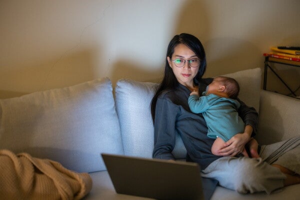 Asian mom checks how to get a PSA birth certificate on her laptop with her baby on her chest.