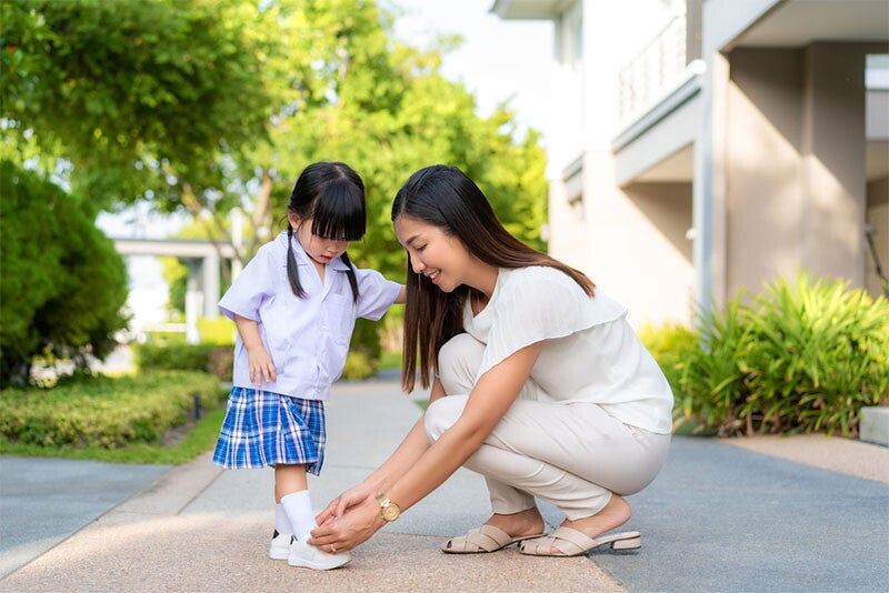 Asian mom helping daughter put on uniform.