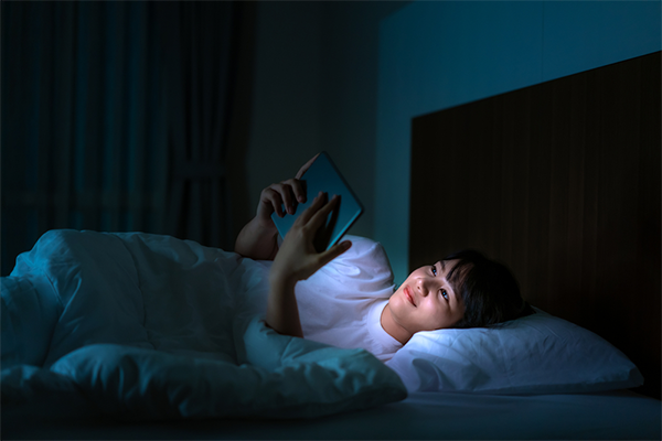 : Asian mom in bed watches a show from her list of K-dramas to watch before going to sleep