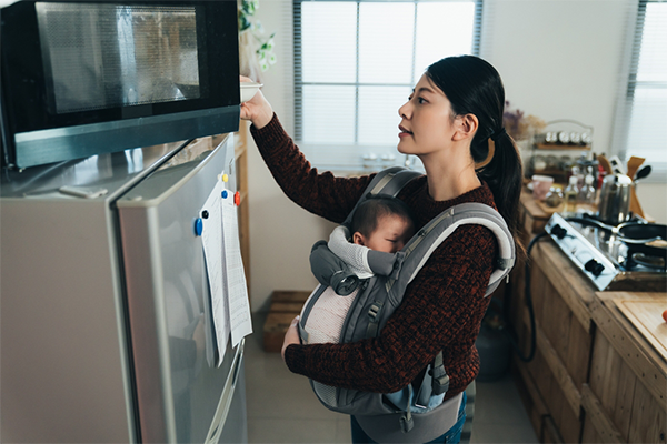 Asian mom performs household tasks with her little one in a baby carrier.