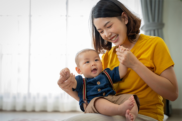 Asian mom plays with her baby son's hands as he sits on her lap.