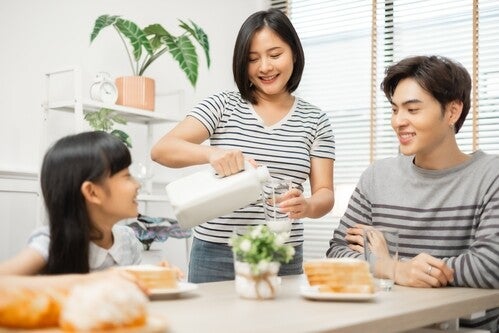 Asian mom pouring a glass of milk for her daughter during breakfast with dad