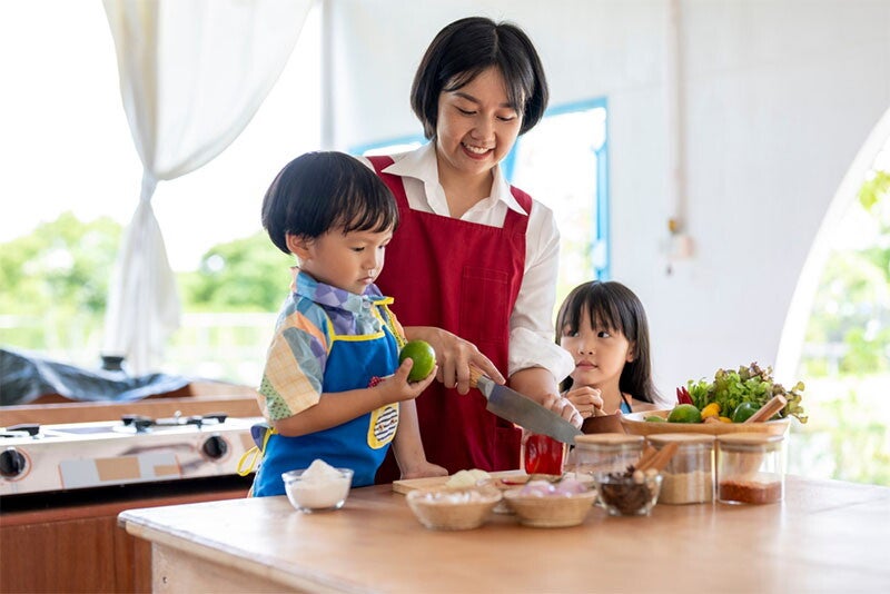 : Asian mom prepares a healthy meal in the kitchen with her two young kids helping her