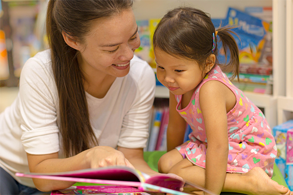 Asian mom reads to her toddler daughter at a public library.