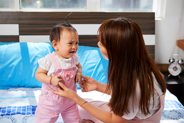 Asian mom talks to her short-tempered little one while they're on a bed.