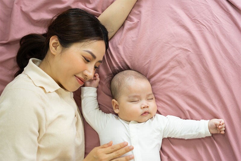 Asian mom watches over her sleeping baby in bed