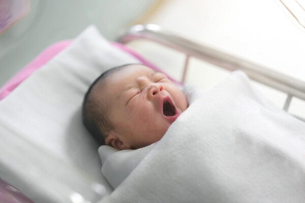 Asian newborn baby yawns as they lie in a bassinet at a maternity hospital.