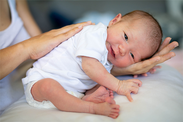 Asian newborn with their back up gets burped on their mother's lap.
