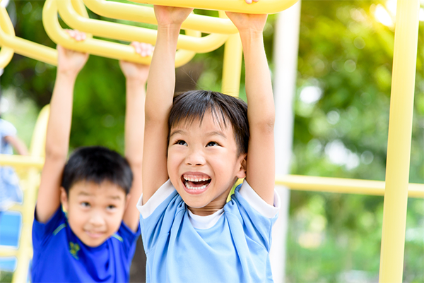 Asian preschool-aged boys test young muscles at the monkey bars.