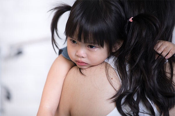 Asian toddler girl rests her chin on her mom's shoulder as she recovers from baby diarrhea.