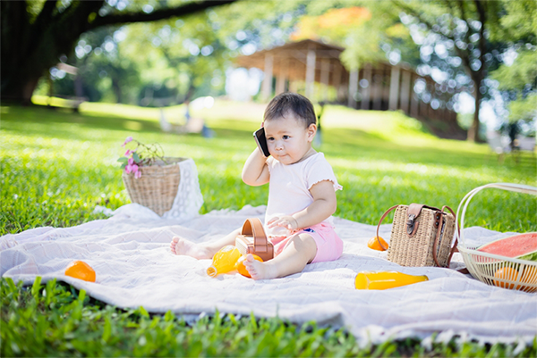 Asian toddler pretending to talk to someone on the phone at the park.