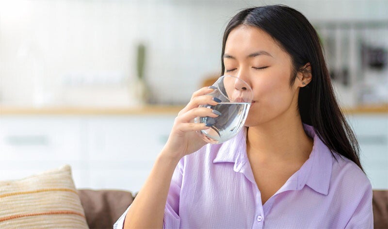 Asian woman drinking a glass of water at home