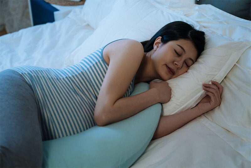 Asian woman pregnant at 38 weeks sleeps on her side using a pillow to support her belly