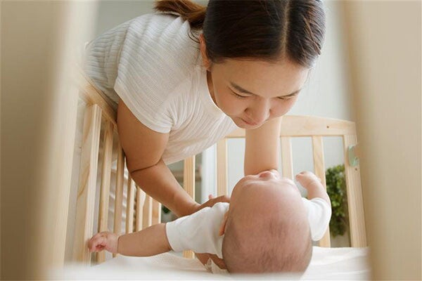Asian woman setting down her newborn in a crib