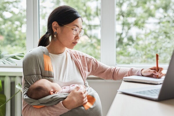 Asian working mom with her little one in a baby carrier writes in her journal. 