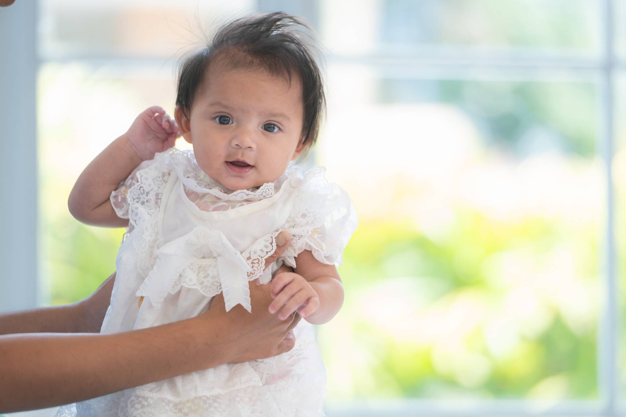 Cropped photo of hands holding a baby girl in a white baptism and christening dress.