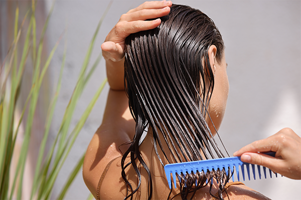 Photo of a woman combing her wet hair with a wide-tooth comb.