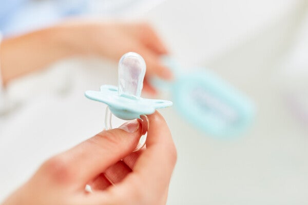 Hands holding a pacifier over a sink for cleaning.
