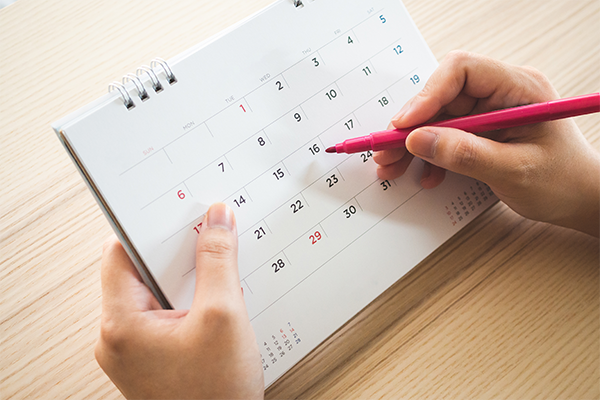 Close-up of a hand holding a pink pen to mark a calendar on a table