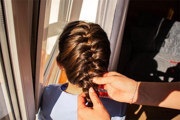 Close-up of a mother’s hand fixing her daughter’s French braid, a cute kid's hairstyle