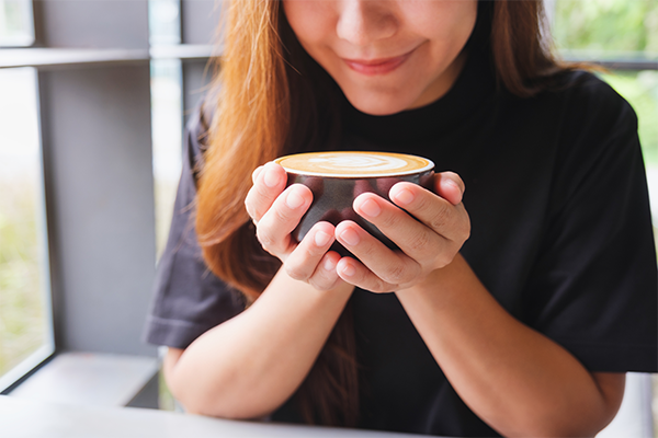 Close-up of a woman holding a cup of coffee at home.