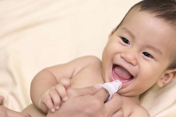 Close-up photo of a mom’s finger massaging the gums of her Asian baby using a clean, boiled gauze