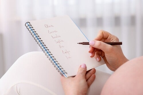 Close-up photo of a pregnant woman’s hand writing down baby girl names in a notebook