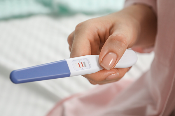 Close-up photo of a woman’s hand holding a positive pregnancy test