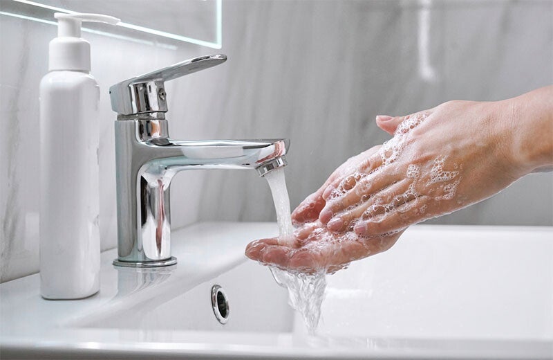 Close-up photo of soapy hands under running water from a bathroom sink.