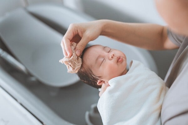 Cropped photo of a mom gently washing her newborn’s hair to help manage cradle cap in babies.