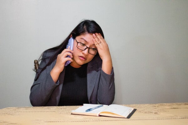 A young Filipina on the phone with a notebook in front of her on the table, trying to speak with a social worker.