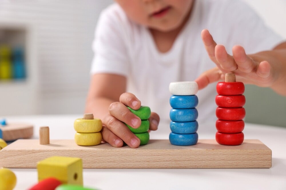 Cropped photo of a little boy stacking and sorting toy rings by color.