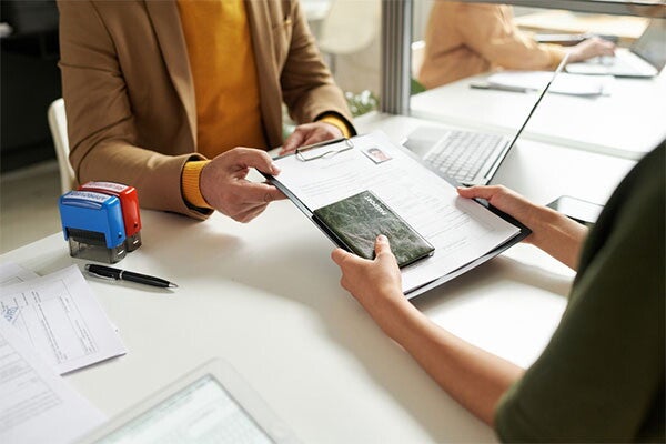 Cropped photo of a woman’s hands giving her family’s passport application forms to another person.