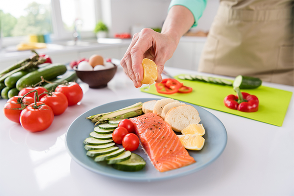 Cropped photo of a woman’s hands squeezing lemon juice onto a plate of salmon and vegetables ready for cooking.