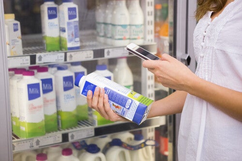 Cropped photo of a young woman holding a milk carton and taking a picture of the nutrition label on the back