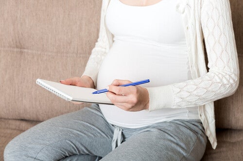 Cropped shot of a pregnant woman’s body sitting on the sofa at home, writing down Korean boy names in a notebook