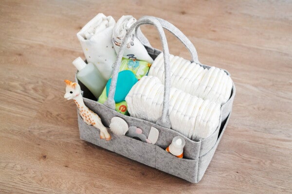 A baby diaper bag filled with diapers, a toy, wipes, a brush and comb, and cloth covers.