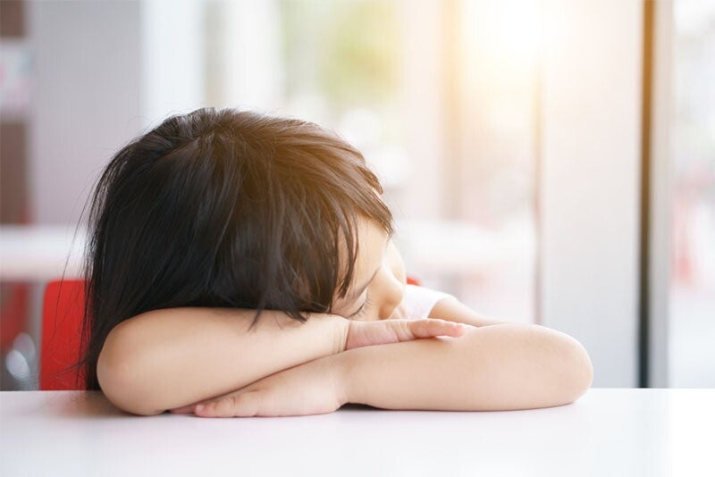 Extremely tired little Asian girl, falling asleep in the classroom at nursery pre-school