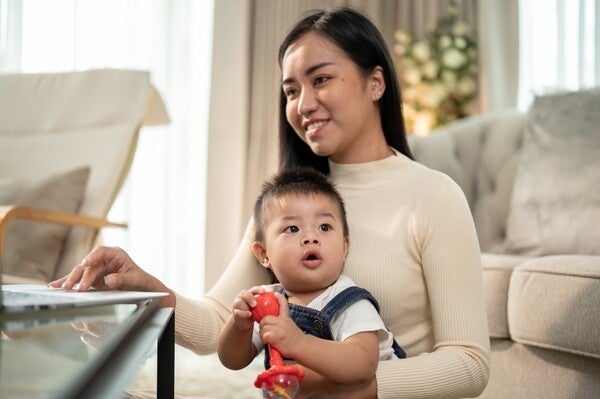 A Filipino mom on her laptop with her child on her lap, researching solo parent requirements.