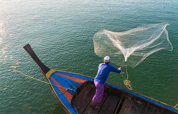 Fisherman throwing a net in water.