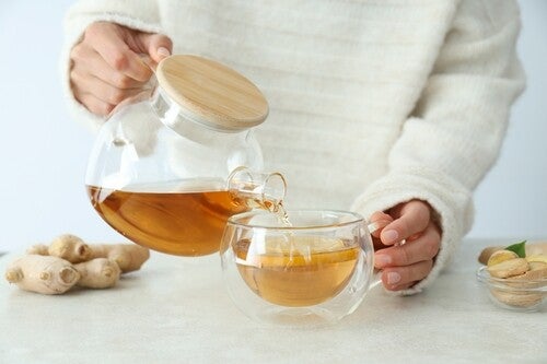 Half-body shot of a woman pouring freshly made ginger tea from a pot to a cup against white background